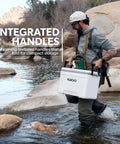 Person carrying Latitude Marine Ultra White 25 Quart Cooler With Cool Riser Technology ThermoCool Foam Insulation in rocky stream.