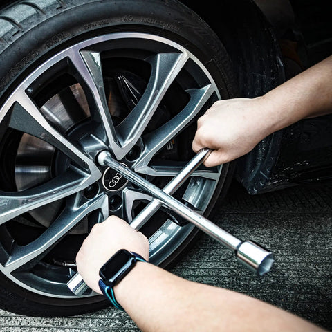 Hands using Heavy Duty Four Way Universal Cross Lug Wrench Tire Iron on a car wheel, showcasing its 14 inch length and chrome plated finish.