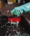 Gloved hand using red 150 lb pull heavy duty handle magnet to lift metal bolts from a tray, auto shop setting.