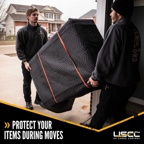 Two movers carrying a heavy duty black polyester moving blanket for protecting furniture during relocation.