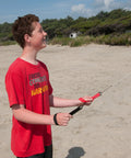 Person flying Dual Line Stunt Parafoil Kite With Tie Dye Style No Assembly Required on a beach, holding braided kite line winder.