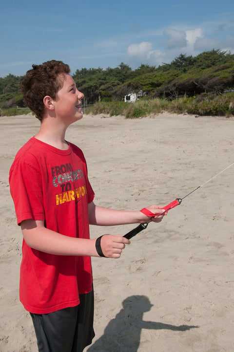 Person flying Dual Line Stunt Parafoil Kite With Tie Dye Style No Assembly Required on a beach, holding braided kite line winder.