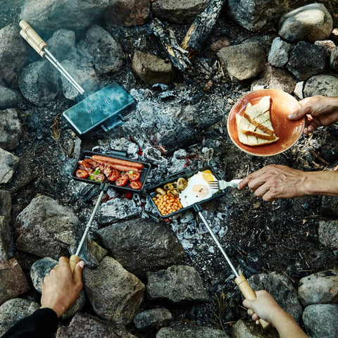 XL Cast Iron Pie Iron Sandwich Maker For Campfire Cooking with food over an open fire, showcasing outdoor use.