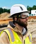 Man wearing MX500 Safety Goggles With 23 Percent Gray Tint and hard hat on construction site, outdoor visibility focus.