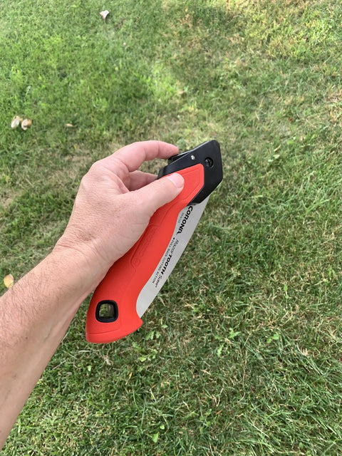 7 Inch Folding Pruning Saw With Fast Cut Razor Tooth Blade Heavy Duty Hand Tool held in hand over grass for tree branch trimming.