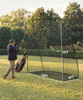 Man practicing golf swing using Heavy Duty Golf Practice Net 10x7 Feet with Sturdy Frame and Quick Setup in backyard lawn.