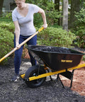 Person using Heavy-Duty 10-Tine Bedding Fork With 48-Inch Hardwood Handle And Cushioned End Grip to move mulch near wheelbarrow.