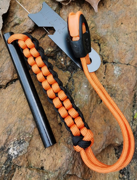 Drilled Ferro Rod Fire Starter Kit with 4 Inch Flint Steel Paracord Lanyard Handle Striker and Whistle on rock surface