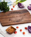 Front view: Wooden cutting board with dark wood finish, laser-engraved Samantha & David and 2022, laurel border.