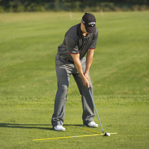 Golfer practicing with two 48 inch golf alignment sticks swing trainer yellow set of 2 with portable storage tube on grass range.