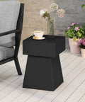 Jack Outdoor Modern Side Table In Matte Black With Lightweight Concrete Build Clean Geometric Design Patio Ready Garden Friendly Minimalist Yet Sturdy Side Table For Couches Decks And Balcony Lounging positioned next to a chair and potted plants