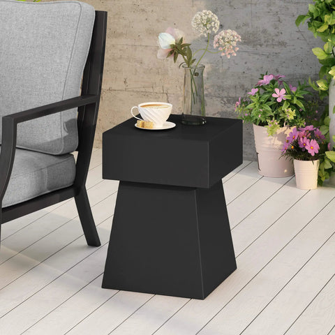 Jack Outdoor Modern Side Table In Matte Black With Lightweight Concrete Build Clean Geometric Design Patio Ready Garden Friendly Minimalist Yet Sturdy Side Table For Couches Decks And Balcony Lounging positioned next to a chair and potted plants