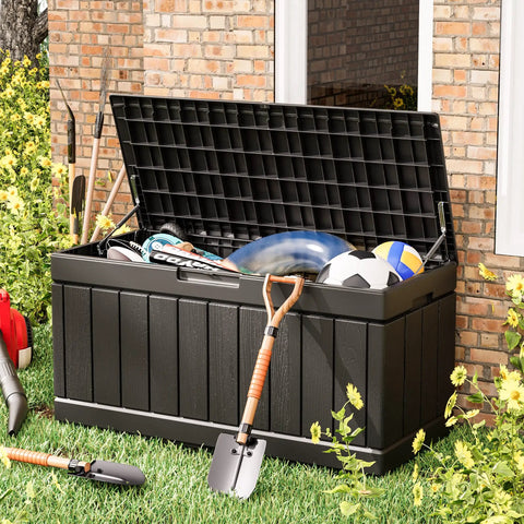Black 82 Gallon Resin Outdoor Storage Box open with garden tools and sports equipment on grass