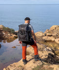 Person hiking with Alta Sky 62 Camera Backpack For 200 To 600mm Telephoto On DSLR Or Full Frame Mirrorless on rocky coast.