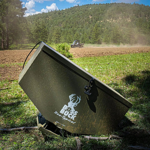 ATV Broadcast Spreader With Wireless Control And Adjustable Flow 80 lb Capacity in a field with tractor in the background