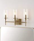 Brass Gold Modern Farmhouse LED Vanity Light Sconce with Clear Glass Cylinder Shade installed above a mirror