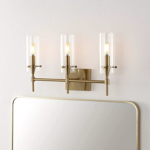 Brass Gold Modern Farmhouse LED Vanity Light Sconce with Clear Glass Cylinder Shade installed above a mirror