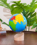 Montessori Color Globe 8.7 Inch Beechwood World Globe With Continent Outlines on a wooden table, surrounded by plants.