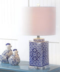 Blue and white chinoiserie ceramic table lamp with white linen drum shade on blue table beside decorative ceramic birds.