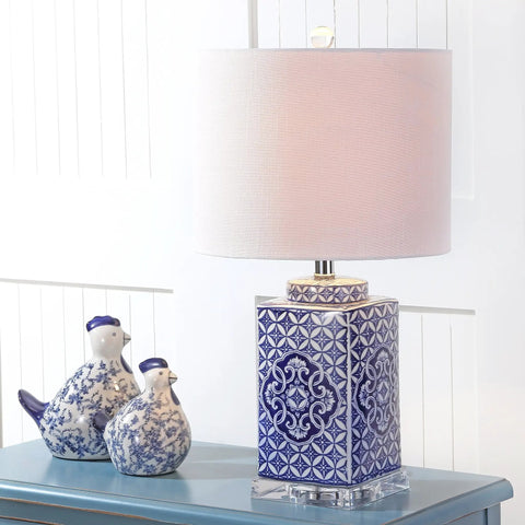 Blue and white chinoiserie ceramic table lamp with white linen drum shade on blue table beside decorative ceramic birds.