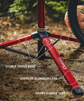 Pro Mechanic HD Bike Repair Stand With 360 Degree Clamp Beefy Heavy Duty Aluminum Build Tripod Base Lightweight Yet Steady Supports Up To 100 Lb Bikes And E Bikes Red showing red tripod base with oversized aluminum legs and rubber feet outdoors