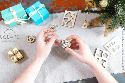 Four In One Wooden Puzzle Kit With Self Assembly Mini Mechanical Models Set Including Stocking Stuffer, Christmas Tree, Clock, And Bauble For Stress Relief, 3D Puzzles Fun For Ages 5 To 80, Plywood Construction, hands assembling round wooden ornament