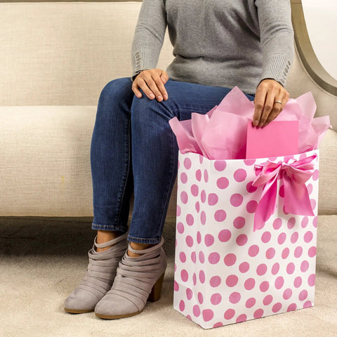 Extra Large Gift Bag With Tissue Paper In Pink Polka Dots And Bow next to seated person, showcasing effortless gifting