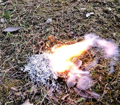 Emergency Fire Starter Kit With 6 Magnesium Shaving Packs And Waterproof Windproof Matches In A Metal Tin igniting on grass