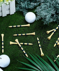 500 Pcs Bamboo Golf Tees 3-1/4 Inches Long Wooden Tees For Golf Practice On The Course Natural Color With Blue Stripes Stable Durable Teeing Accessories Pack scattered on grass with golf balls and greenery.