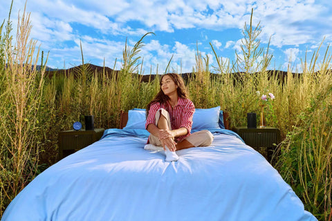 Woman sitting on bed outdoors with Take Anywhere Portable Bluetooth Speaker With WiFi Alexa Built In 24 Hour Battery Life Wireless Charging Base.