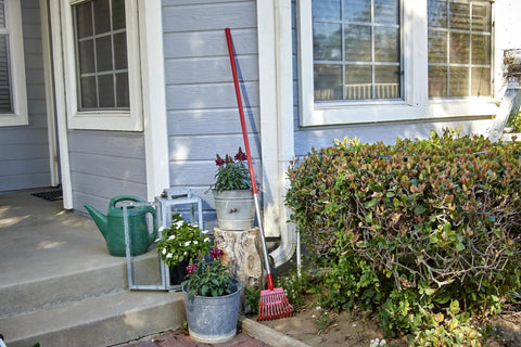 Fixed Tine Shrub Rake With Aluminum Handle 8 Inch Wide resting against a garden wall near shrubs and outdoor plants