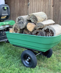Dumping Lawn And Garden Utility Trailer With 6.5 Cubic Foot Poly Tray, carrying firewood, attached to a lawn mower in a garden setting.