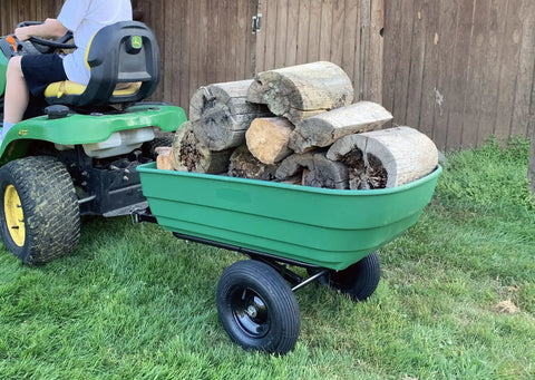 Dumping Lawn And Garden Utility Trailer With 6.5 Cubic Foot Poly Tray, carrying firewood, attached to a lawn mower in a garden setting.