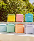 Colorful coolers displayed outdoors, including a Powder Blue 11 Qt Tag-Along Two Strapped Picnic Style Cooler With Hands Free Crossbody Strap.