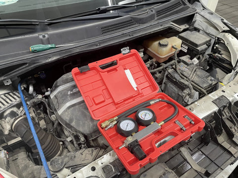 Front view of red HFS cylinder leak detector test kit with dual gauges and hoses on engine bay