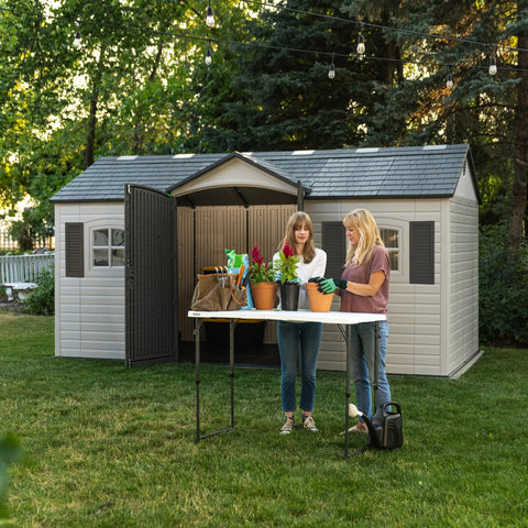 Two people gardening in front of Desert Sand Outdoor Storage Shed 15x8 Ft Resin Backyard Tool Shed With Lockable Doors.