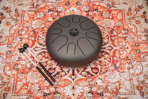 Super Responsive 16 Inch Steel Tongue Drum With Eight Soothing Notes on a patterned rug, includes pro grip mallets.
