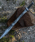 Hand Forged Knight Sword In Spring Steel 35 Inch Full Tang resting on wooden log outdoors.