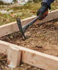 Using IsoCore Pickaxe Mattock With Shock Absorbing Handle Dual Head For Roots And Rocks 1.5 Lb Heavy Duty Tool on soil beside wood frame