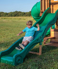Child sliding down the wave slide of the Cedar Cove Wooden Swing Set with Spiral Tube Slide and Wave Slide, Elevated Clubhouse, in a backyard.