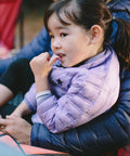 Child in a blue puffy jacket sitting outdoors, showcasing the comfort and warmth suitable for camping and outdoor activities.