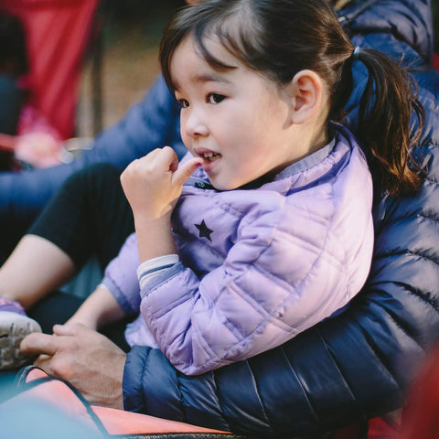 Child in a blue puffy jacket sitting outdoors, showcasing the comfort and warmth suitable for camping and outdoor activities.
