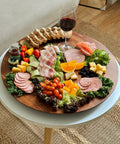 21 Inch Acacia Wood Lazy Susan For Tabletop Giant Round Turntable Serving Tray Next Level Charcuterie And Cheese Boards Platter Extra Large Organizer For Countertop Kitchen Revolution with assorted meats, cheese, and vegetables.