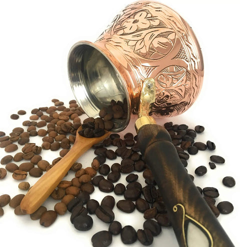 Dope Thick Solid Copper Turkish Greek Arabic Coffee Pot With Wooden Handle For Stovetop Brewing Jazzve Cezve Ibrik Briki Café Turco Large 18 Oz Engraved Design Authentic Turkish Coffee Maker with coffee beans spilling from it.