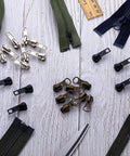 Size 5 Zipper Repair Kit with 12 sliders, 12 bottom stops, 24 top stops for metal, plastic, and nylon coil zippers on wooden background.