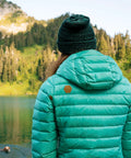 Person wearing jacket with Tenacious Tape Repair Patches Peel And Stick Nylon Gear Patches outdoors near lake and mountains