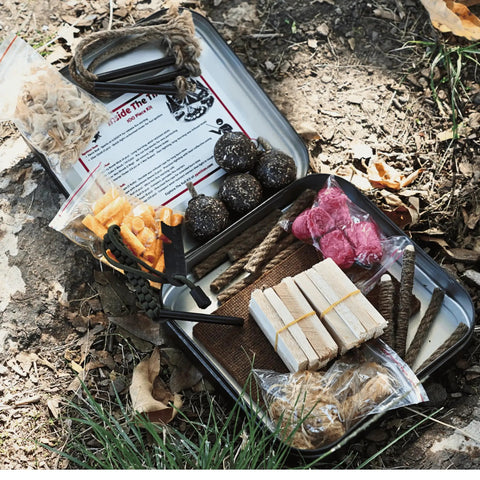 All In One 100 Piece Fire Starter Kit For Campfires And Survival With Ferro Rod 3000F Sparks Char Cloth Wax Ropes Fatwood Fire Cubes Wick Rolls And More The Go To Bushcraft And Camping Fire Kit in a tin box on ground