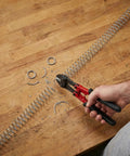 Person cutting Two Pack 0.8mm Wire Compression Springs, 10mm Outer Diameter, 300mm Long, Steel Pen Springs with pliers on table.