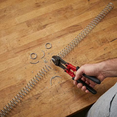 Person cutting Two Pack 0.8mm Wire Compression Springs, 10mm Outer Diameter, 300mm Long, Steel Pen Springs with pliers on table.