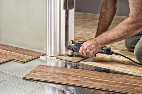 Man using AW400 F80 Sonicrafter 4.2 Amp Oscillating Multi Tool With 9 Accessories to trim wood flooring near a door frame.